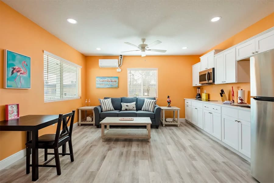 Cozy living area with orange walls, a sofa, a dining table, and a modern kitchen.