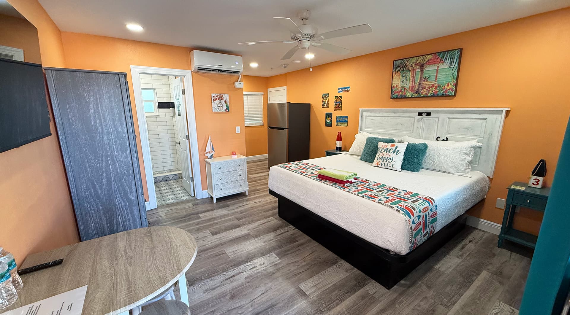 Cozy bedroom with a white bed, colorful decor, and bright orange walls.