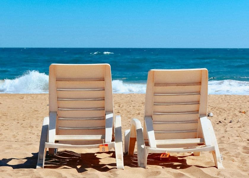 Two white beach chairs on the sand facing the ocean with waves breaking near the shoreline. Two white beach chairs on the sand facing the ocean with waves breaking near the shoreline.