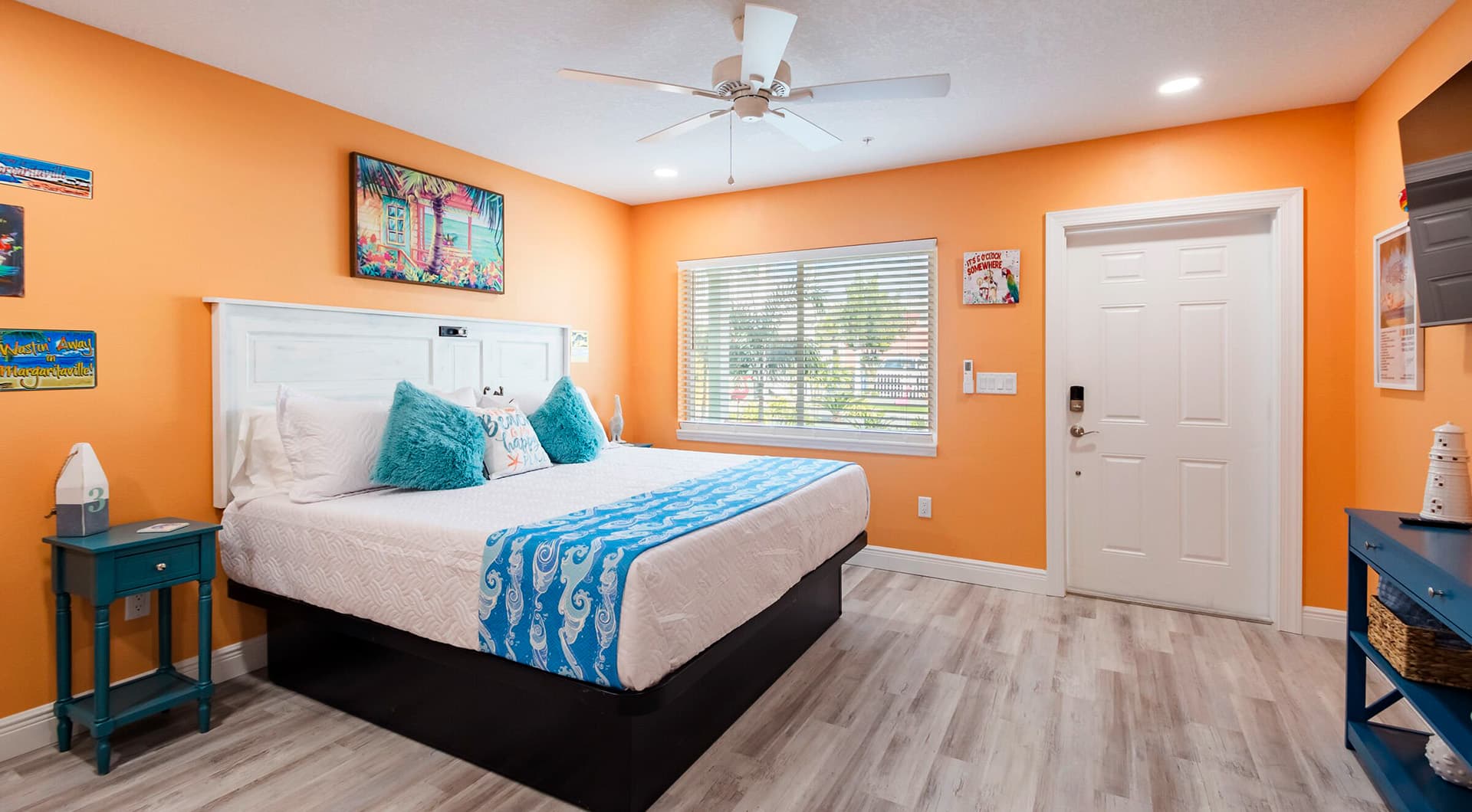 Brightly colored bedroom featuring an orange wall, a king-sized bed with decorative pillows, and a window with blinds.