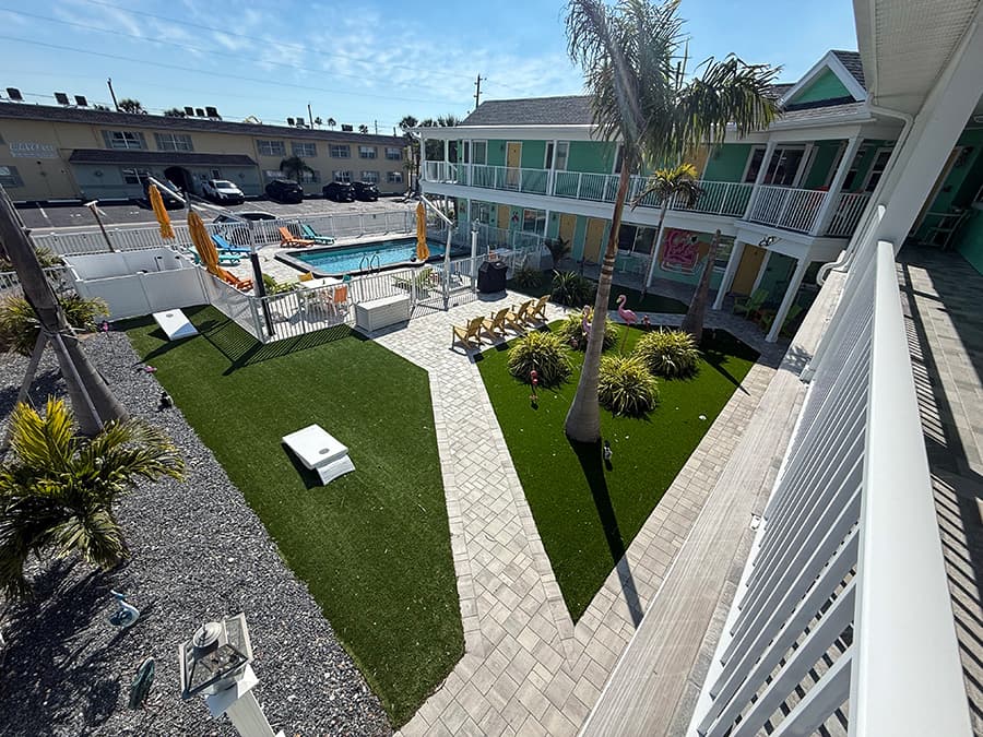 View of a vibrant courtyard with palm trees, lounge chairs, and a pool surrounded by colorful buildings.