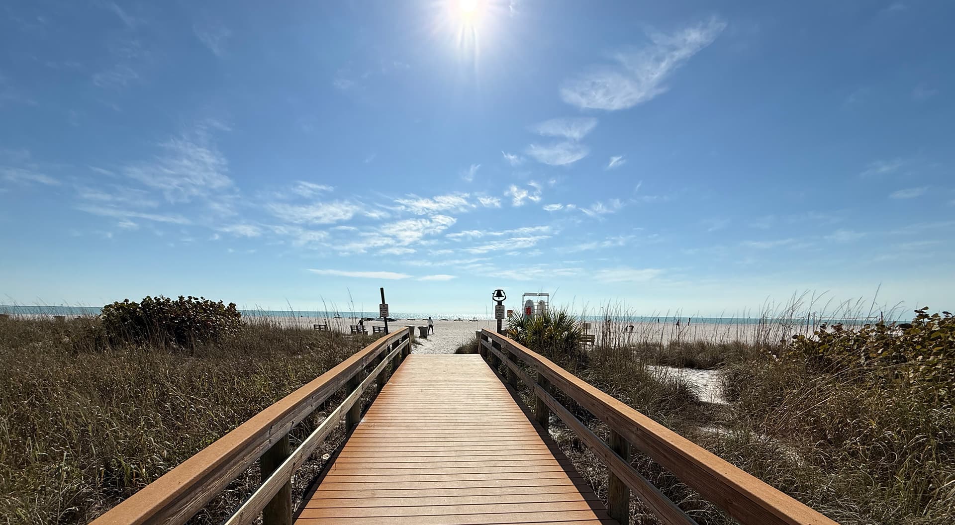 A wooden pathway leads to the beach under a bright blue sky.